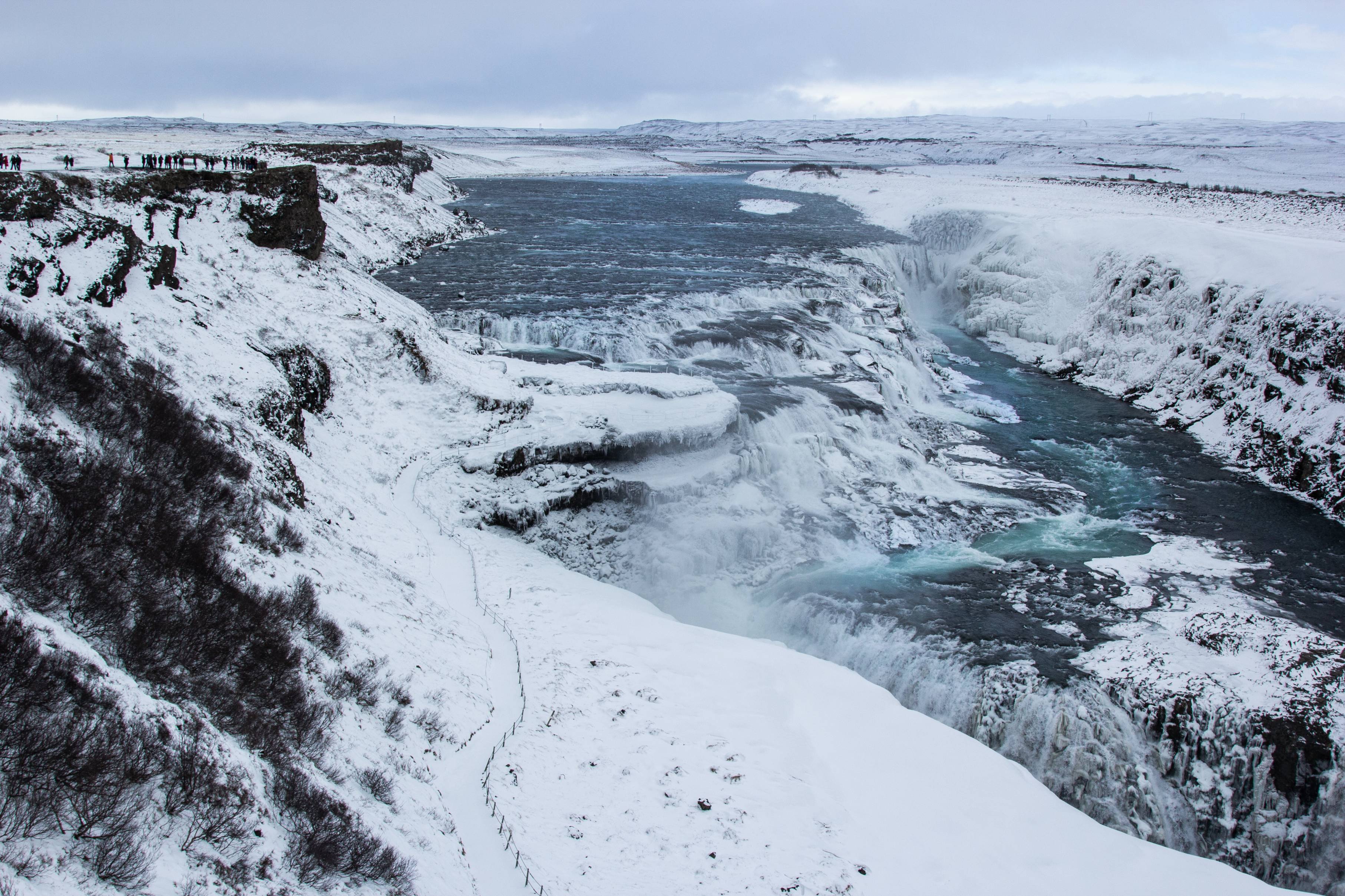 Gullfoss-waterfall-covered-in-snow-with-people-watching-from-a-cliff-side-above-on-the-left