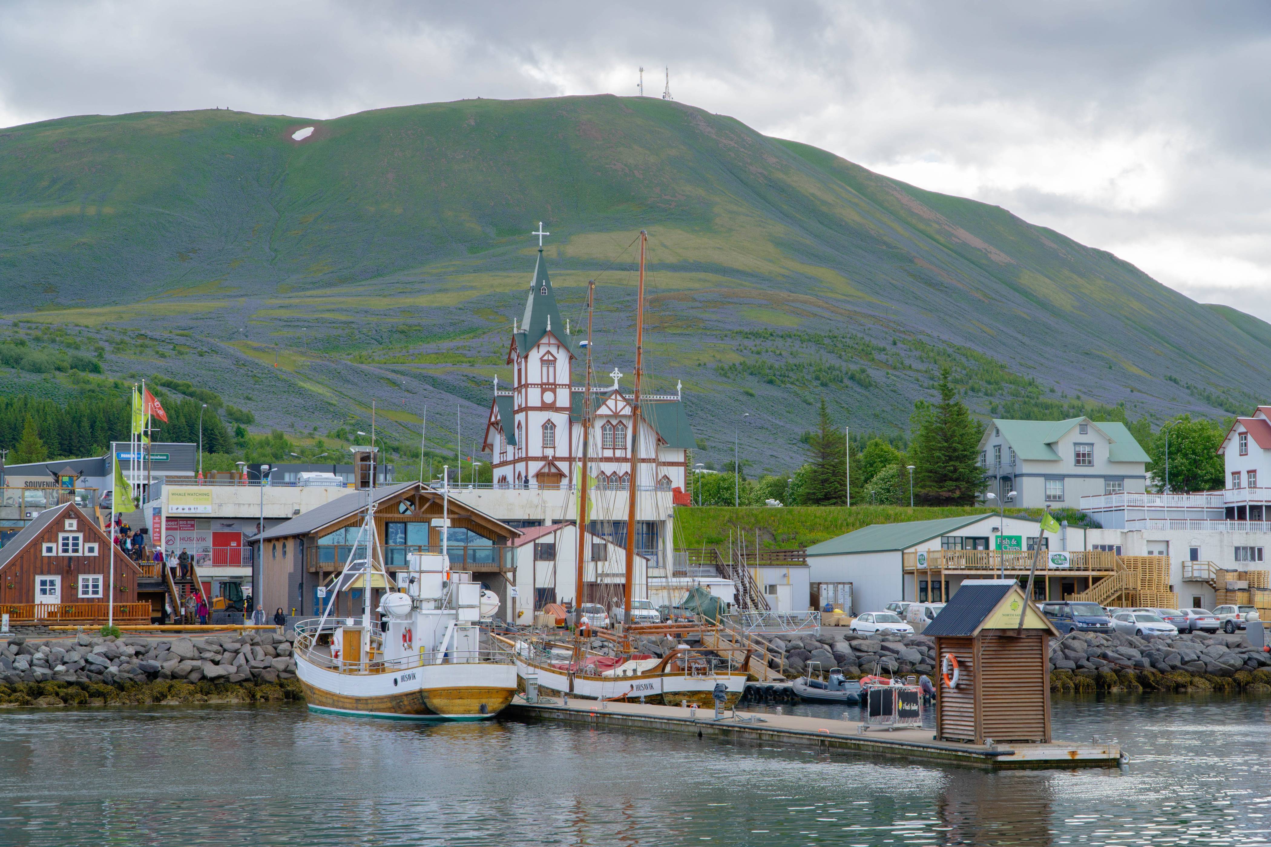 Husavik-harbor-with-two-small-boats-seen-from-the-ocean-with-husavik-church-in-the-background-on-a-summer-day