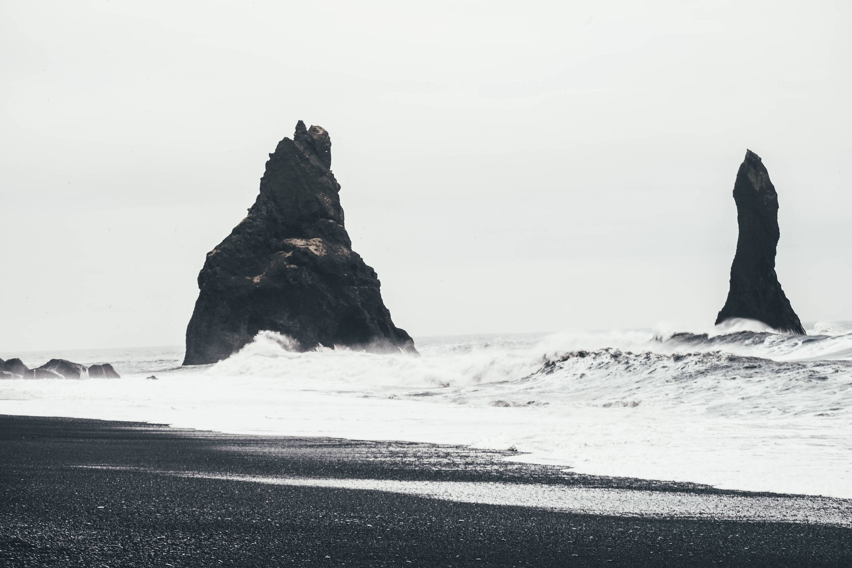 Reynisfjara-black-beach-big-roaring-waves-from-ocean-and-seeing-rocky-sea-stacks-in-background-on-a-moody-cloudy-day