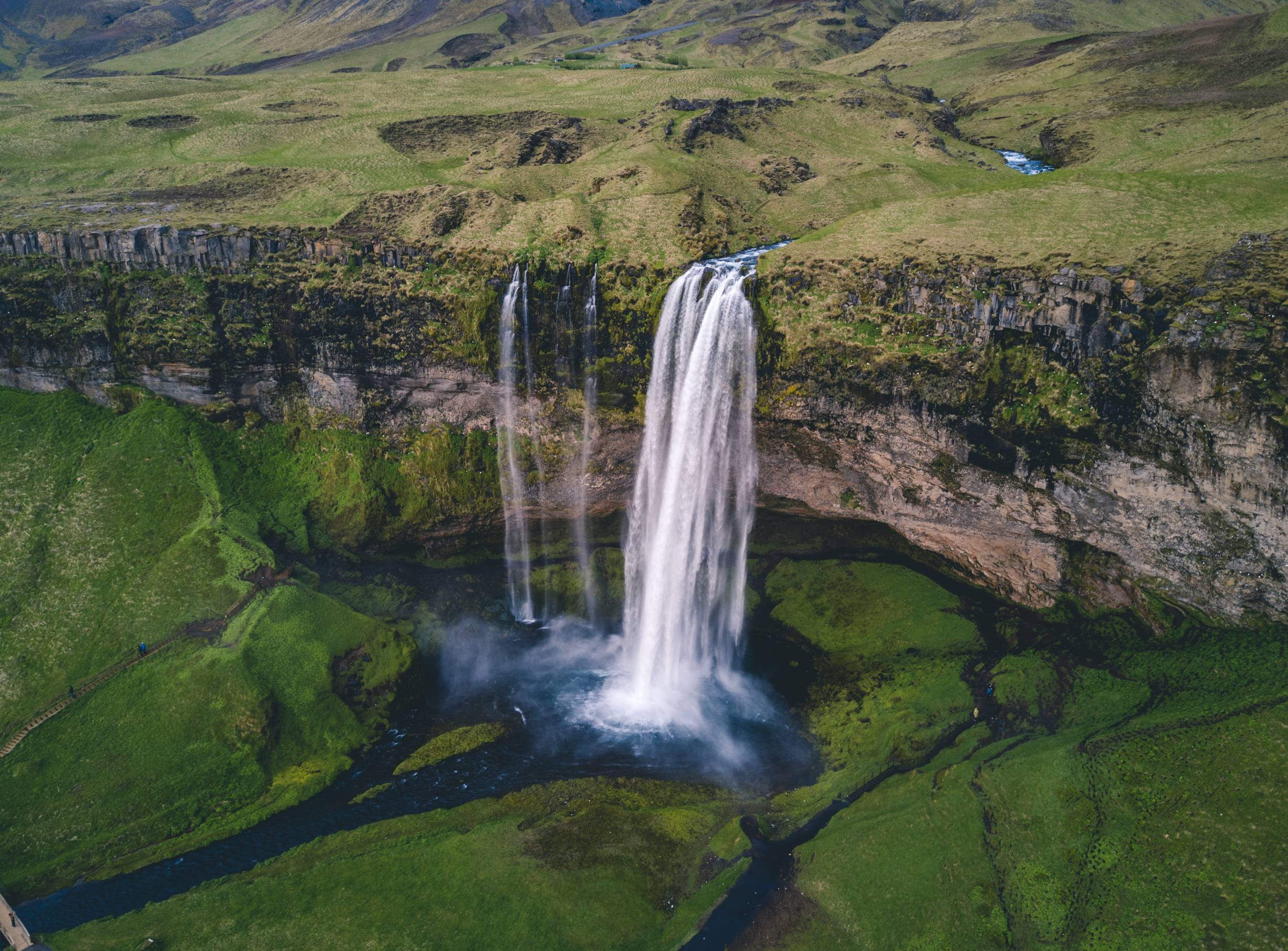 Seljalandsfoss-waterfall-seen-from-a-drone-above-on-a-summer-day-surrounded-by-green-grass