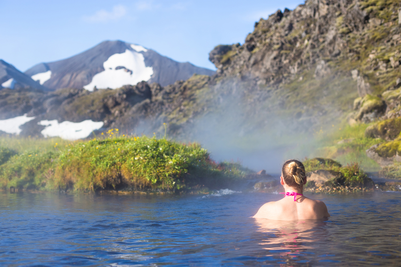woman-relaxing-in-geothermal-hot-spring-in-iceland-during-summer-bright-warm-day-with-green-grass-and-lava-rocks-around