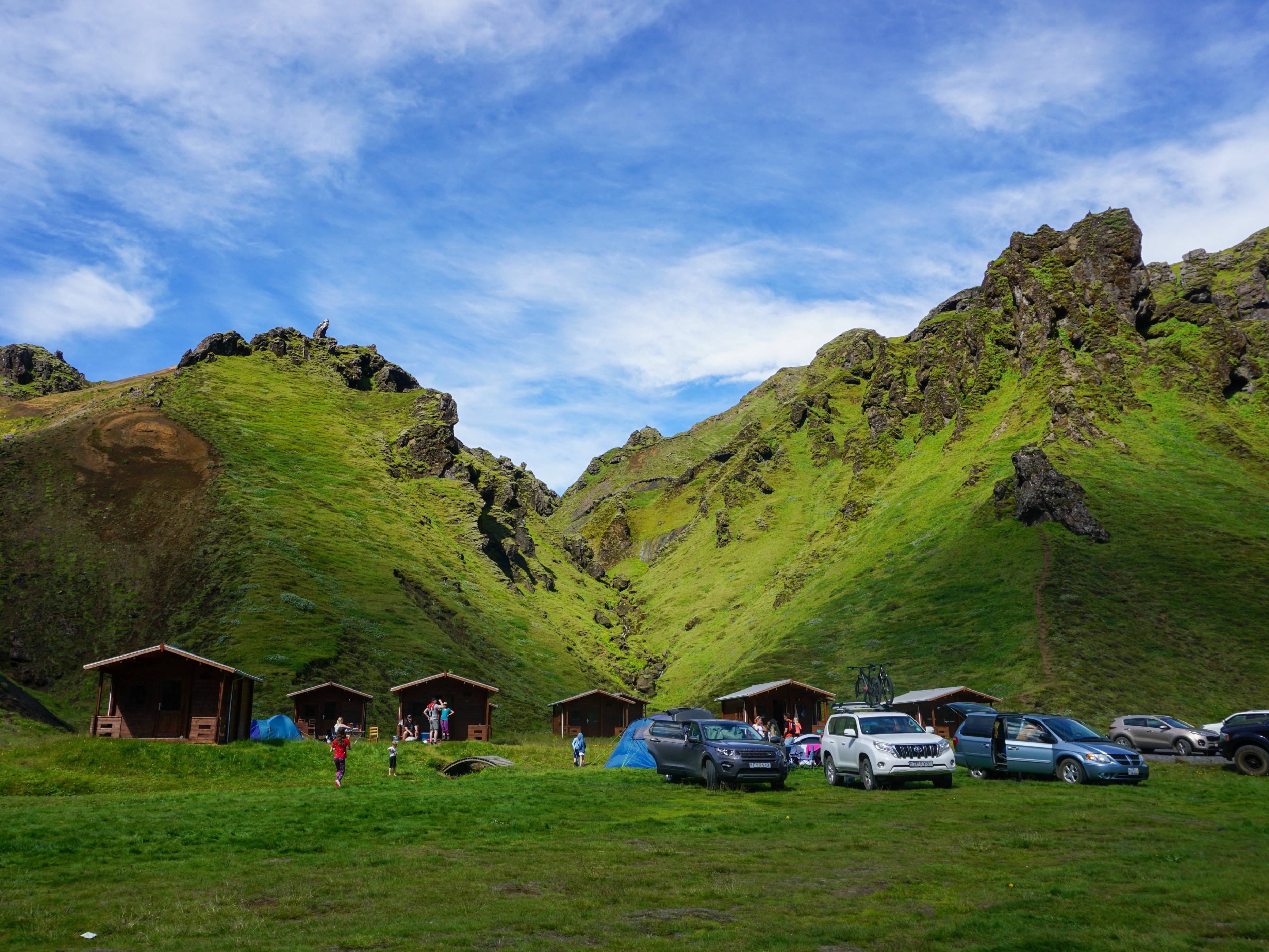 campsite-full-of-people-tents-vehicles-and-a-few-small-cabins-in-Iceland-in-summer-surrounded-by-green-mountains