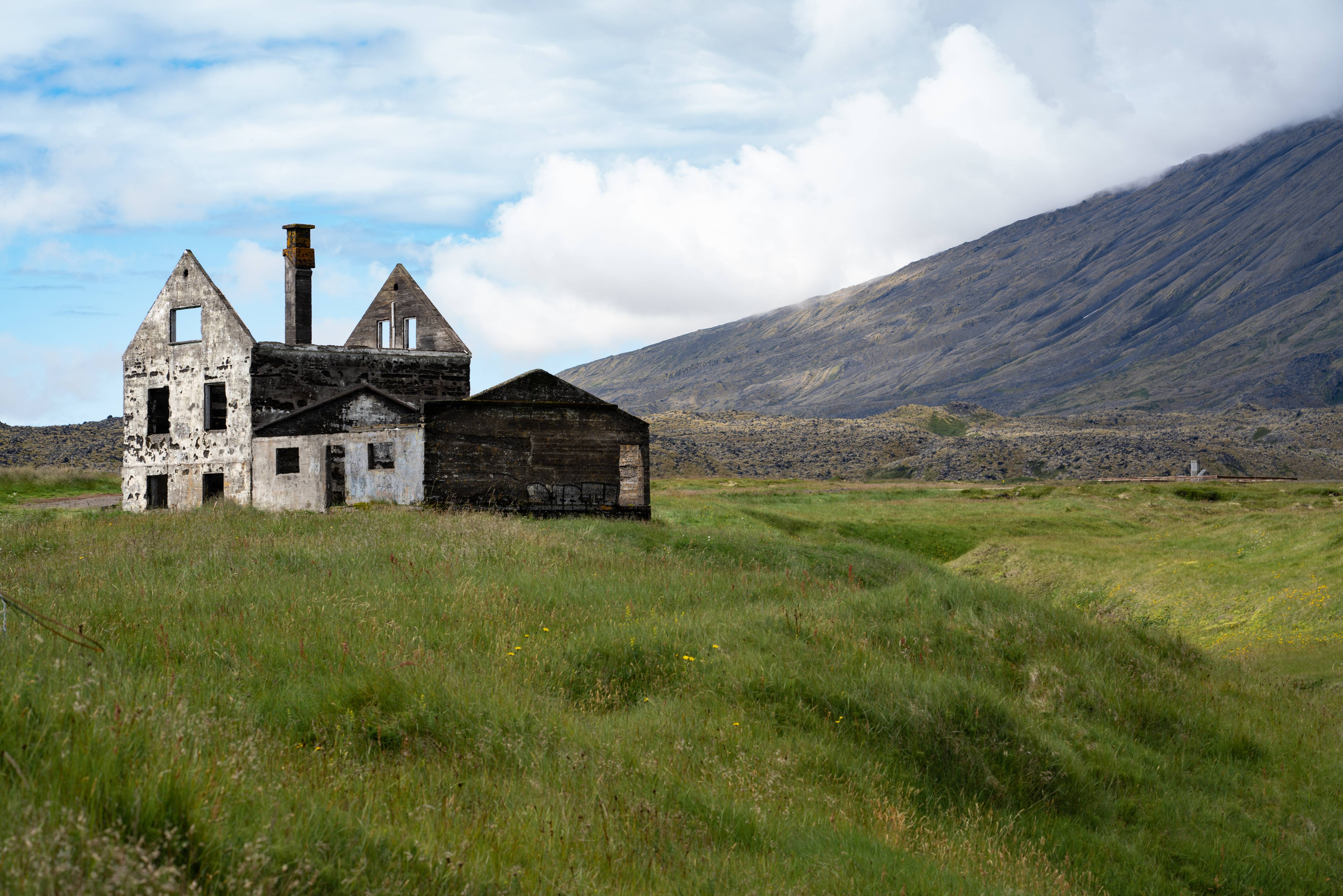 old-run-down-house-in-iceland-on-a-beautiful-summer-day-clear-blue-skies-and-deep-green-grass-around-it-and-a-big-steep-mountain-behind-it