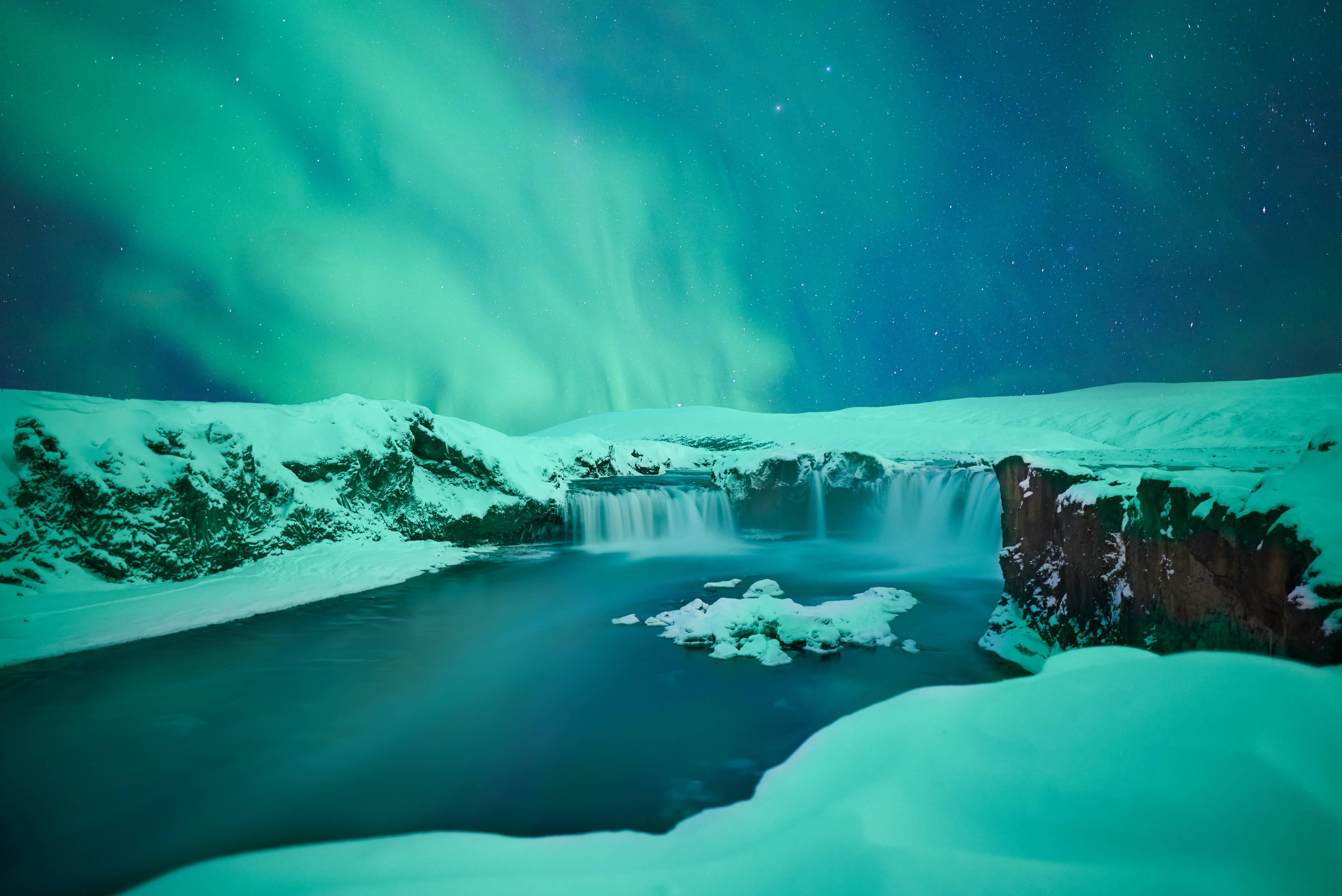 Godafoss-waterfall-in-iceland-in-winter-covered-in-snow-with-northern-lights-green-and-blue-in-the-sky