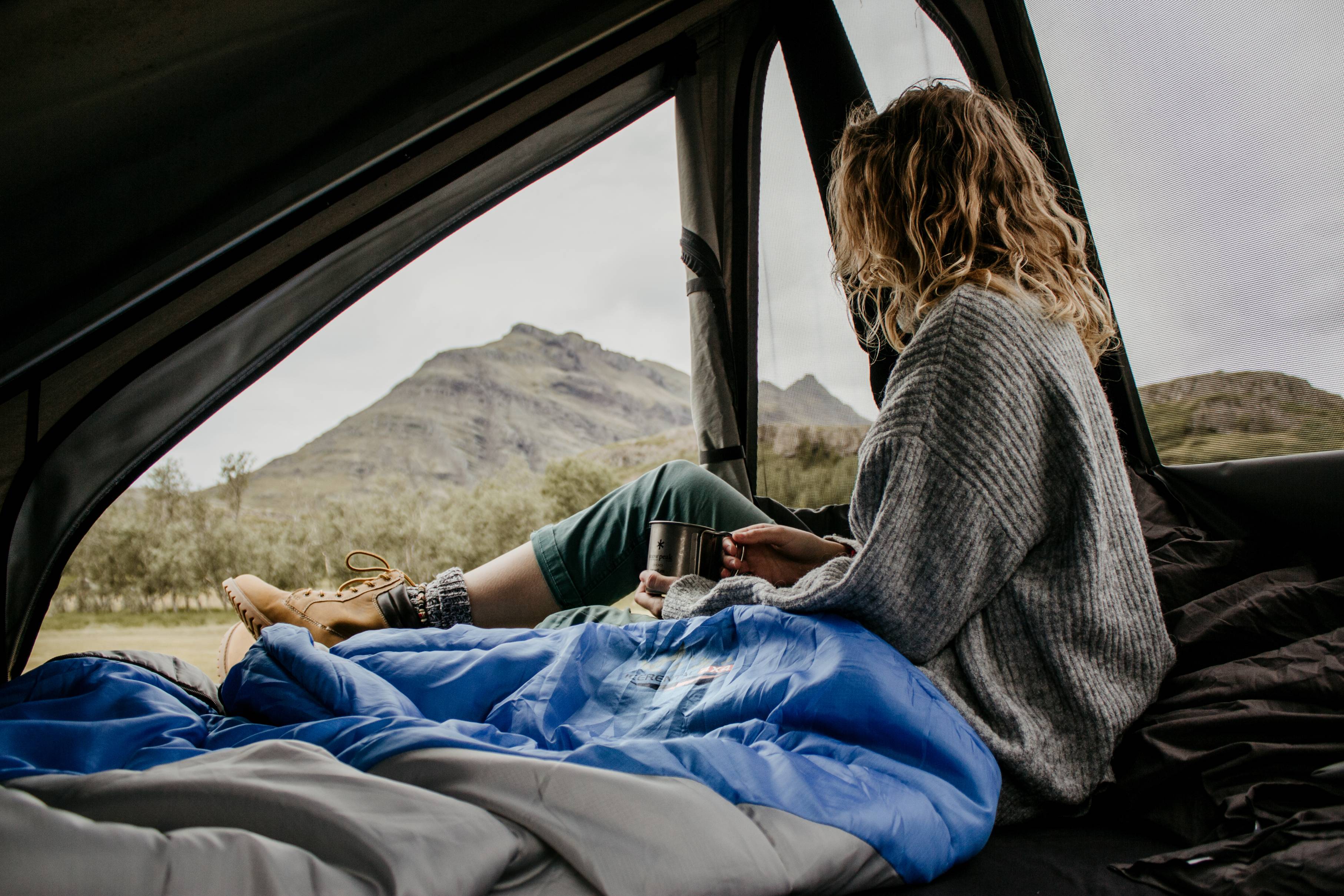 woman-in-a-Icerental-4x4-roof-tent-holding-a-cup-of-coffee-looking-out-on-a-summer-day-in-Iceland